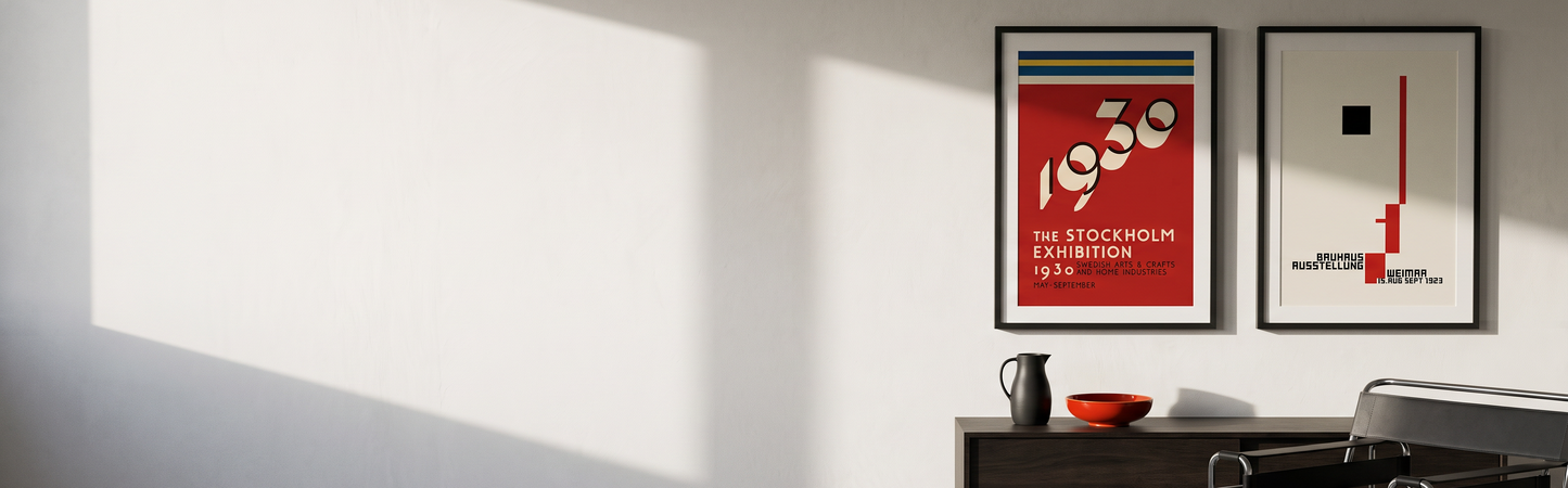 PosterFusion Two framed Bauhaus-era exhibition posters, a red Stockholm 1930 poster and a cream Bauhaus Weimar poster, on a white plaster wall above a dark oak sideboard, light from a window on the left
