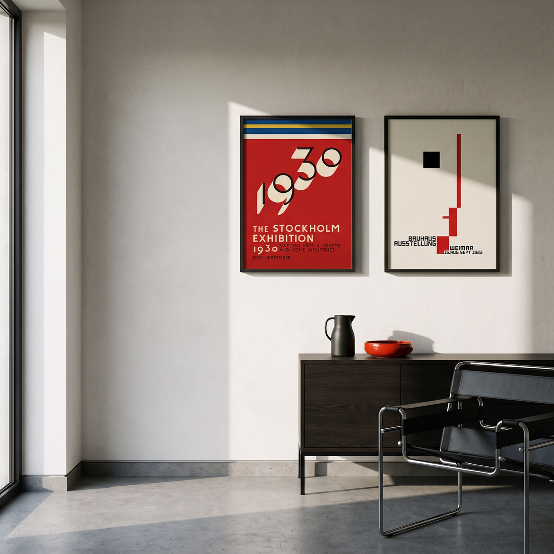 PosterFusion Two framed exhibition posters, a red Stockholm 1930 and a cream Bauhaus Weimar, on a white plaster wall above a dark oak sideboard with a steel chair, window light from the left